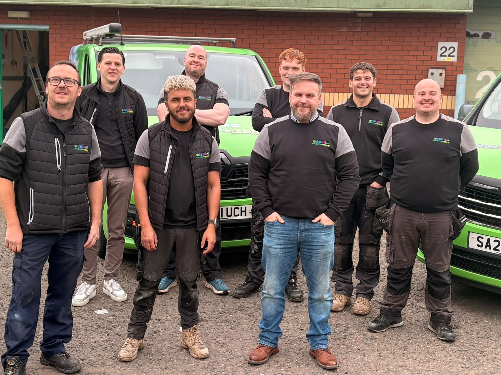 The Energy Made Greener engineering team standing in front of their green branded vans at the EMG unit in Glasgow
